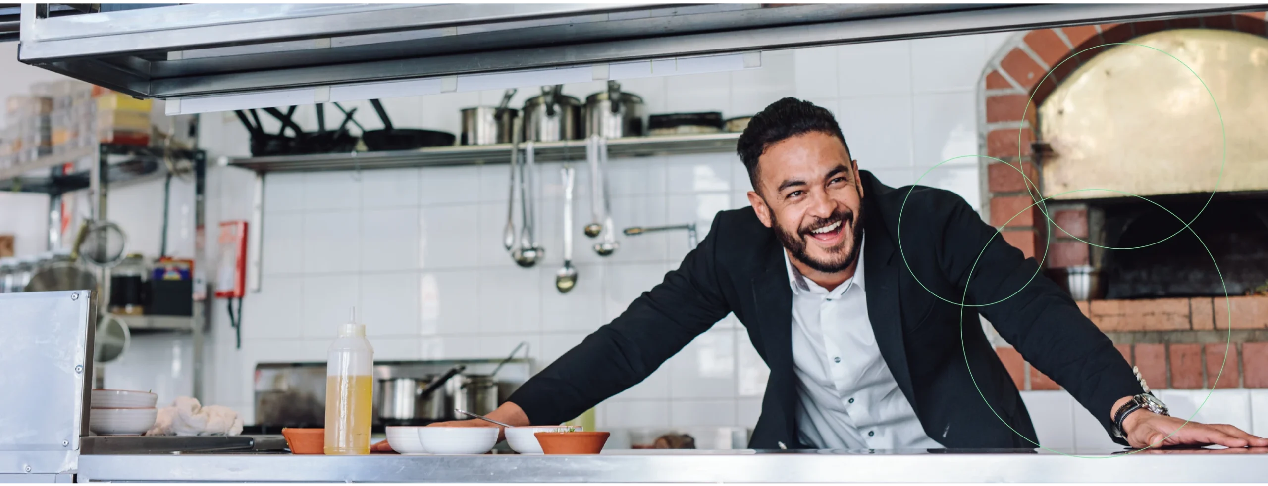Man behind commercial kitchen counter leaning over smiling.
