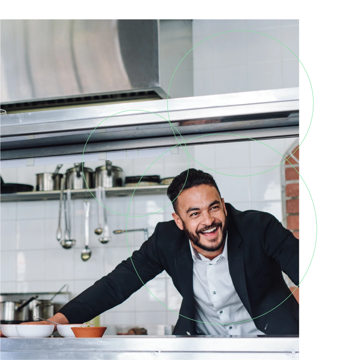 Man behind commercial kitchen counter leaning over smiling.