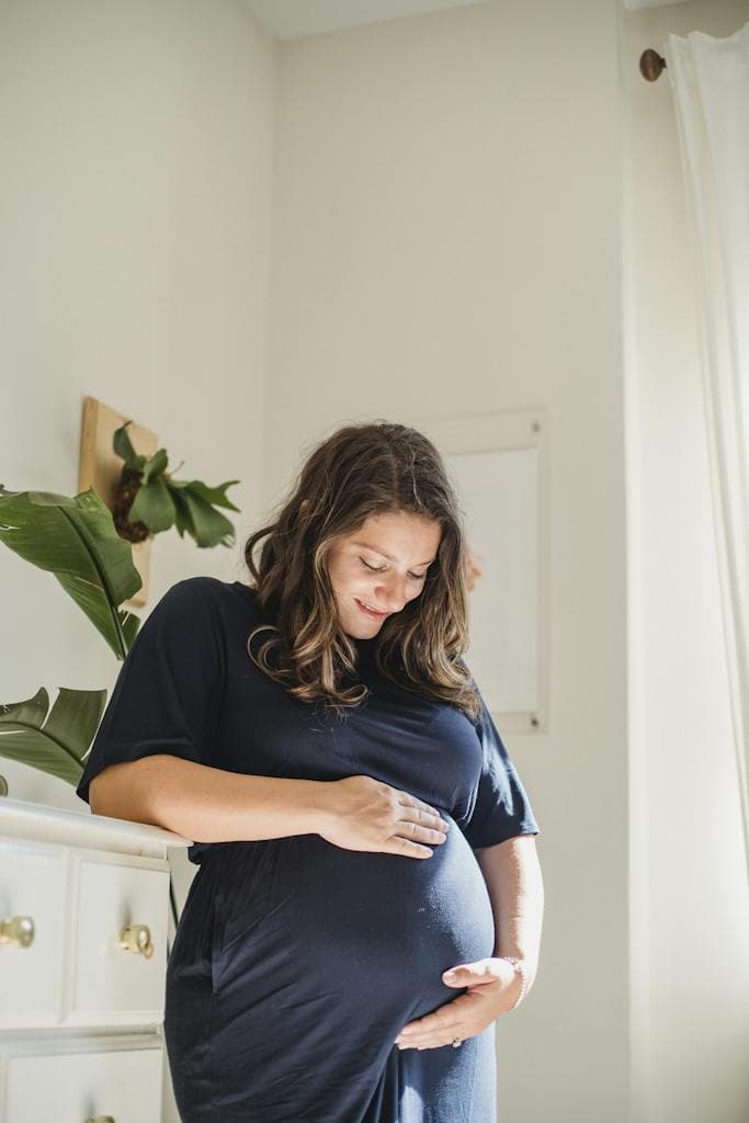 Glad pregnant woman caressing tummy in house room